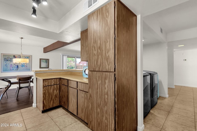 kitchen featuring hanging light fixtures, kitchen peninsula, separate washer and dryer, and light tile patterned floors