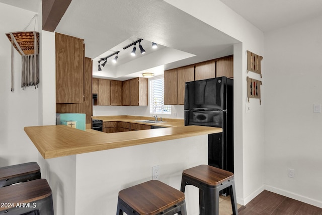 kitchen with a breakfast bar area, dark wood-type flooring, kitchen peninsula, sink, and black fridge