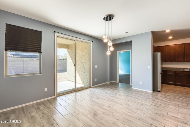 unfurnished dining area with light wood-type flooring and baseboards