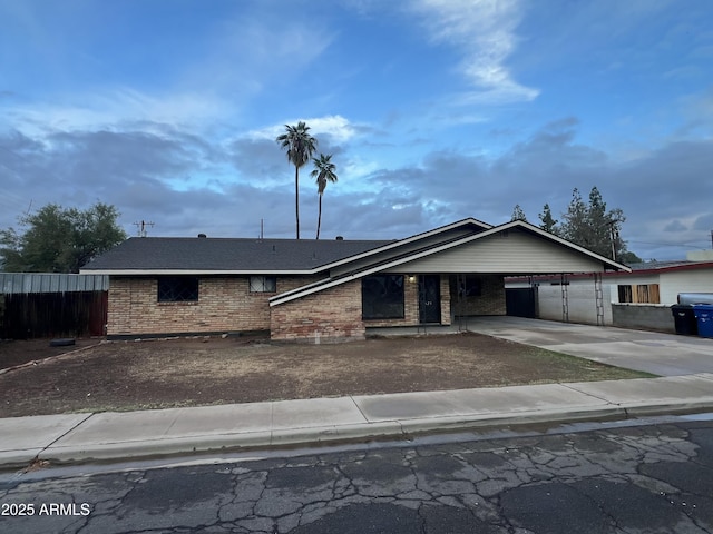 view of front of house featuring concrete driveway, brick siding, fence, and an attached carport