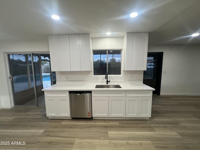 kitchen with stainless steel dishwasher, light wood-type flooring, a sink, and white cabinetry