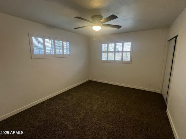 empty room with ceiling fan, baseboards, and dark colored carpet