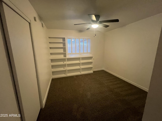 empty room with a ceiling fan, dark colored carpet, and baseboards