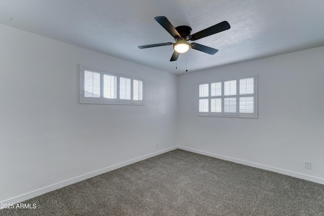 empty room featuring a ceiling fan, dark colored carpet, and baseboards