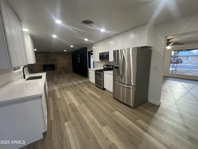 kitchen featuring stainless steel appliances, visible vents, light wood-style floors, a brick fireplace, and a sink