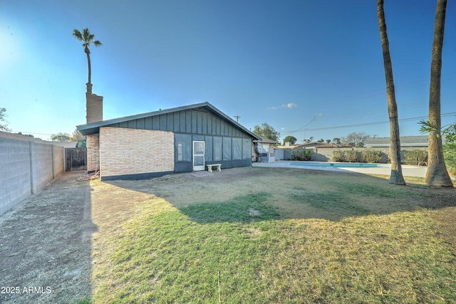 back of property with a fenced in pool, brick siding, a yard, board and batten siding, and fence