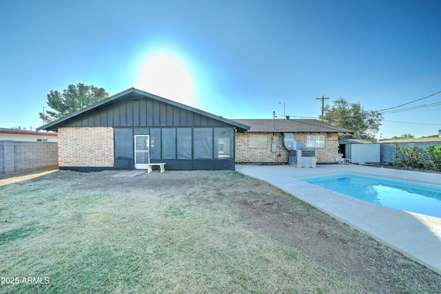 rear view of property featuring a fenced in pool, brick siding, a lawn, board and batten siding, and a fenced backyard