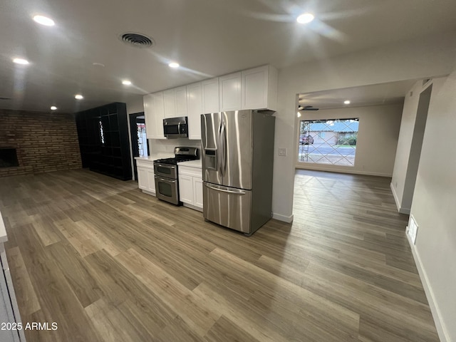 kitchen with visible vents, appliances with stainless steel finishes, open floor plan, white cabinetry, and wood finished floors