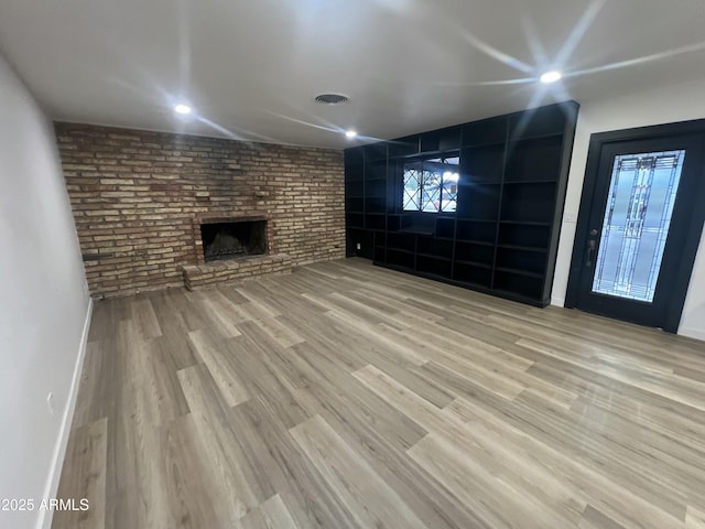 unfurnished living room with brick wall, a fireplace, wood finished floors, visible vents, and baseboards