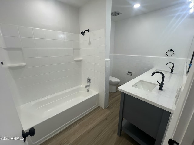 bathroom with visible vents, toilet, wood finished floors, a sink, and tile walls