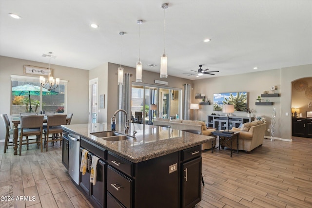 kitchen with sink, ceiling fan with notable chandelier, decorative light fixtures, an island with sink, and dark stone countertops