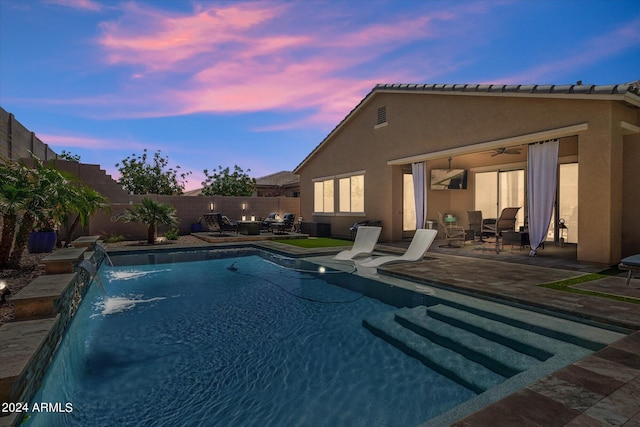 pool at dusk featuring pool water feature and a patio area