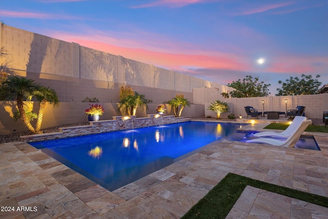 pool at dusk with a patio and pool water feature