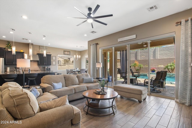 living room with ceiling fan with notable chandelier and light hardwood / wood-style flooring