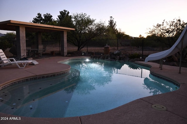 pool at dusk featuring a patio area and a water slide