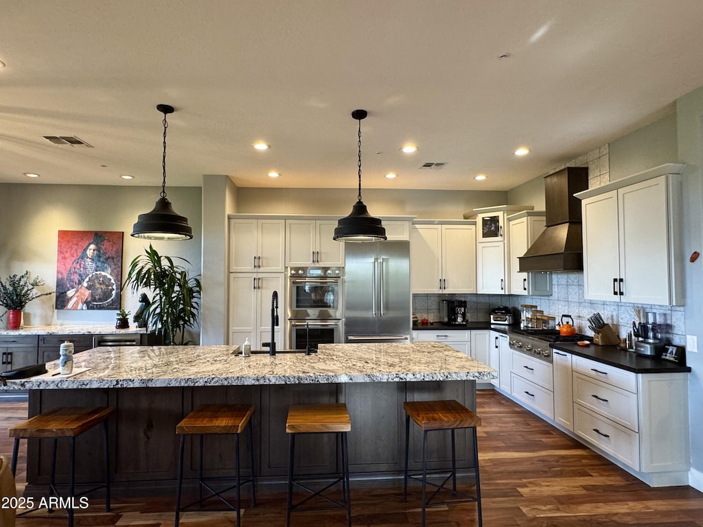 kitchen with tasteful backsplash, decorative light fixtures, a center island with sink, appliances with stainless steel finishes, and custom exhaust hood