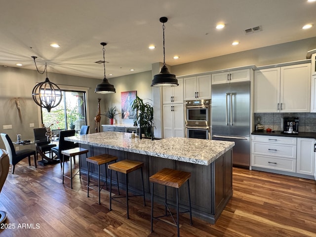 kitchen featuring white cabinets, pendant lighting, stainless steel appliances, and a center island with sink