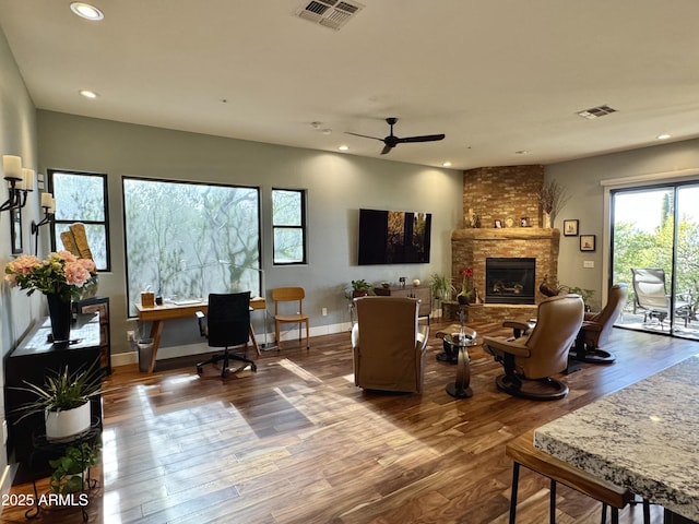 living room with ceiling fan, wood-type flooring, and a brick fireplace