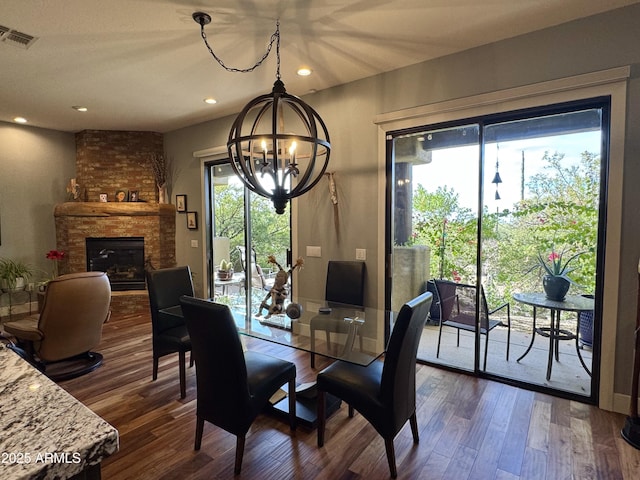 dining space featuring a chandelier, a healthy amount of sunlight, dark hardwood / wood-style flooring, and a brick fireplace