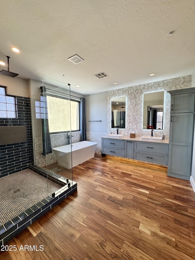 bathroom with plus walk in shower, vanity, wood-type flooring, and a textured ceiling