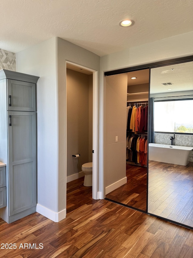 unfurnished bedroom featuring dark hardwood / wood-style floors, a textured ceiling, connected bathroom, and a closet