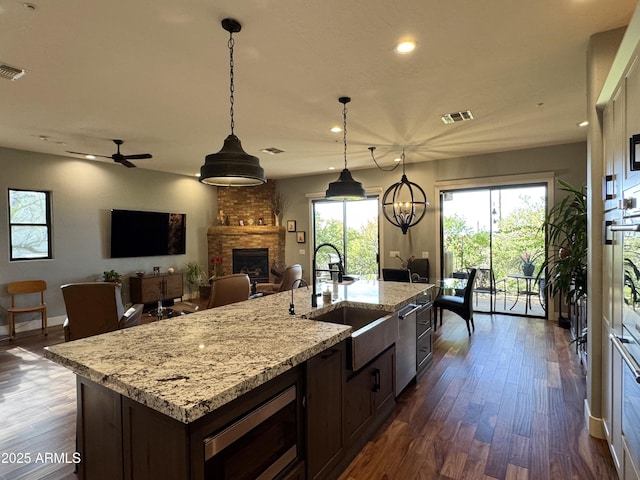 kitchen featuring ceiling fan with notable chandelier, a brick fireplace, decorative light fixtures, dark brown cabinets, and stainless steel appliances