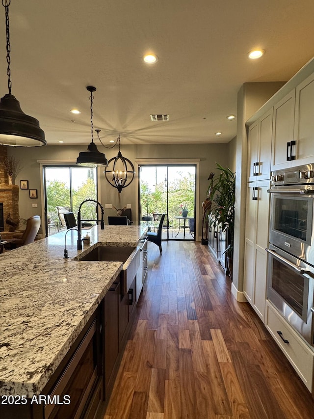 kitchen with hanging light fixtures, light stone counters, dark hardwood / wood-style flooring, stainless steel double oven, and a chandelier