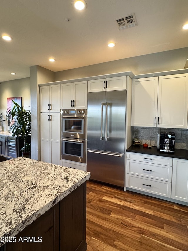 kitchen with backsplash, white cabinets, wine cooler, appliances with stainless steel finishes, and dark hardwood / wood-style flooring