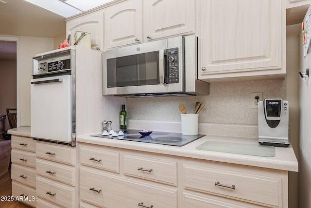 kitchen featuring black electric cooktop, light brown cabinets, white oven, and backsplash