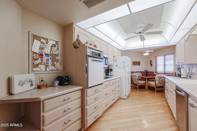 kitchen with appliances with stainless steel finishes, sink, ceiling fan, a raised ceiling, and light wood-type flooring