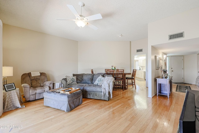 living room with ceiling fan, vaulted ceiling, light hardwood / wood-style floors, and a textured ceiling