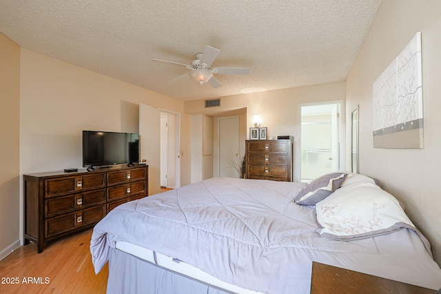 bedroom with ceiling fan, ensuite bath, light hardwood / wood-style flooring, and a textured ceiling