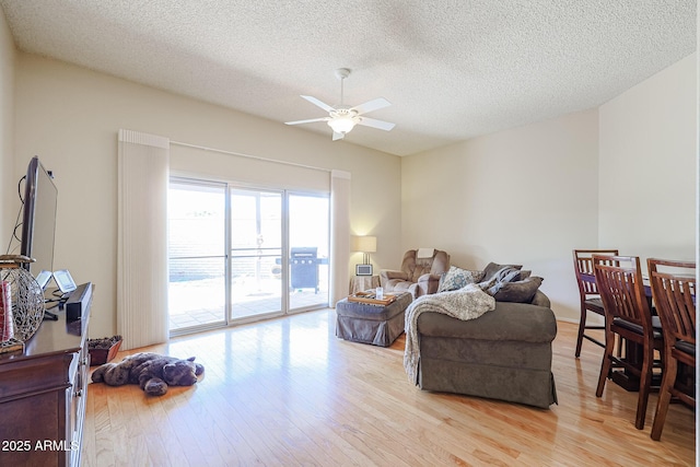 living room with a textured ceiling, ceiling fan, and light wood-type flooring