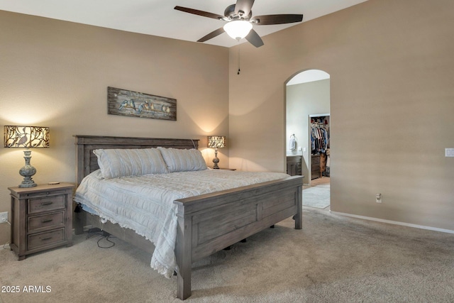 bedroom featuring a closet, arched walkways, baseboards, light colored carpet, and a spacious closet