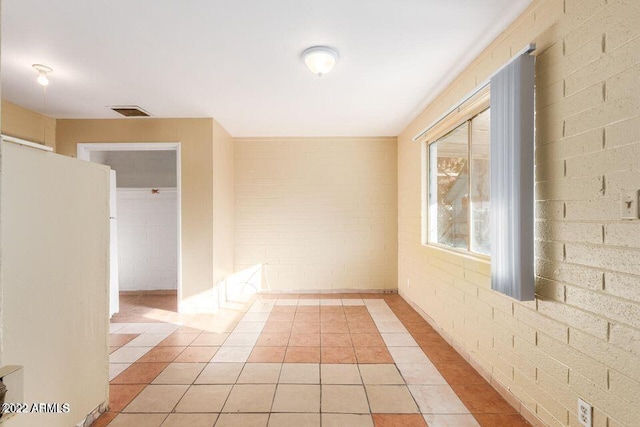 spare room featuring brick wall, visible vents, and light tile patterned flooring