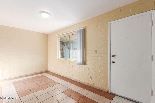 empty room featuring brick wall and light tile patterned flooring