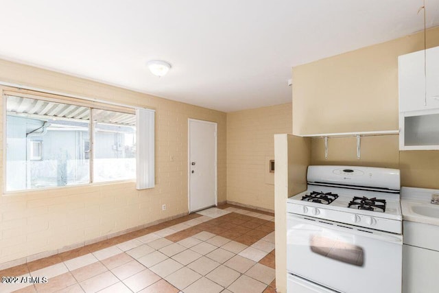 kitchen featuring white gas stove, light tile patterned floors, light countertops, white cabinetry, and a sink