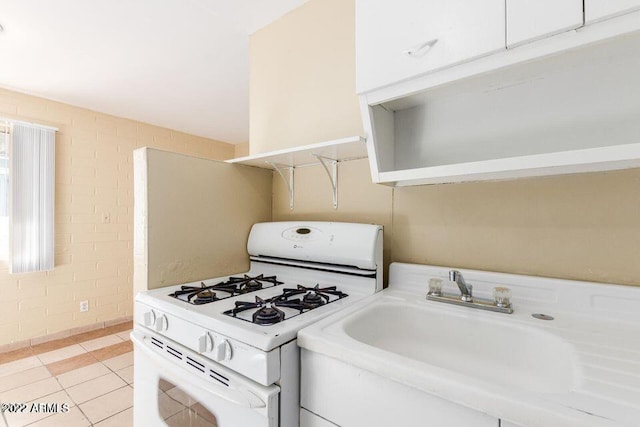 kitchen with light countertops, light tile patterned floors, a sink, and white gas range