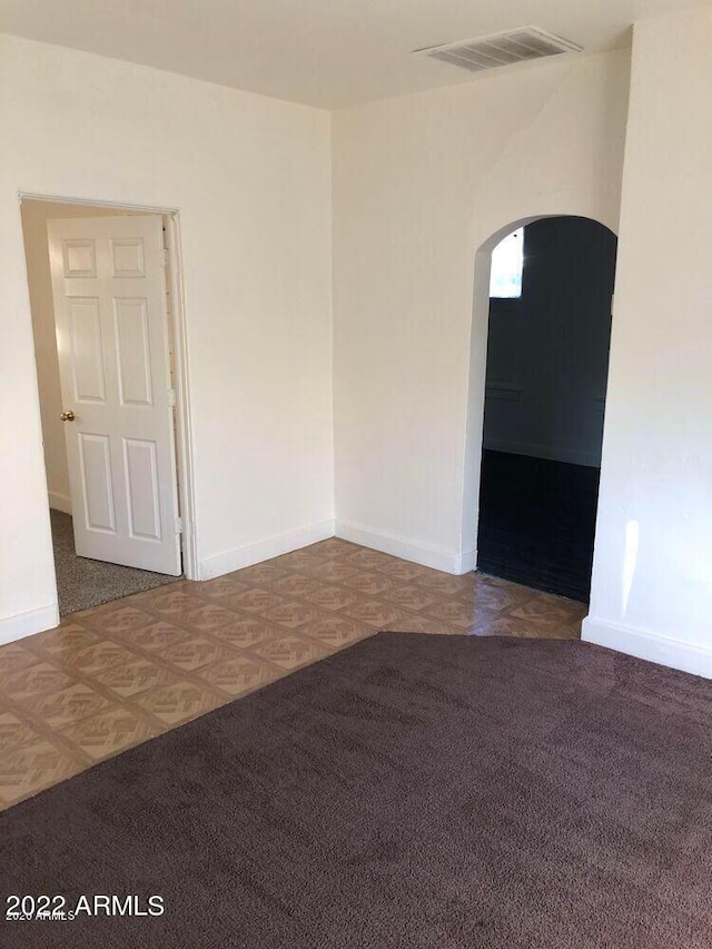 empty room with carpet floors, baseboards, visible vents, and arched walkways