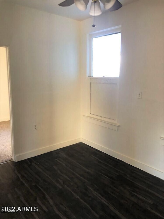 empty room featuring dark wood-type flooring, baseboards, and a ceiling fan