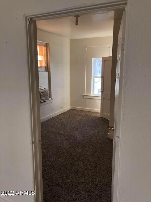 empty room featuring dark colored carpet and baseboards