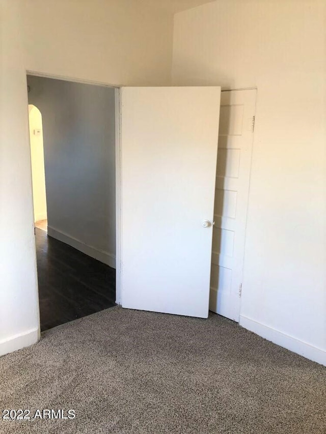 unfurnished room with carpet floors, baseboards, and arched walkways