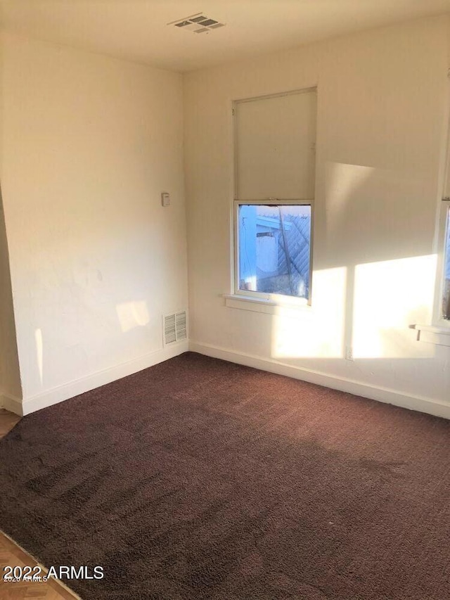 empty room featuring dark colored carpet, visible vents, and baseboards