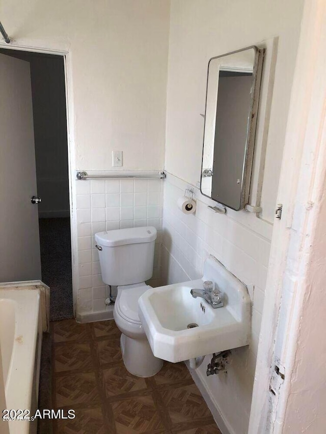 bathroom featuring toilet, a tub, a wainscoted wall, a sink, and tile walls