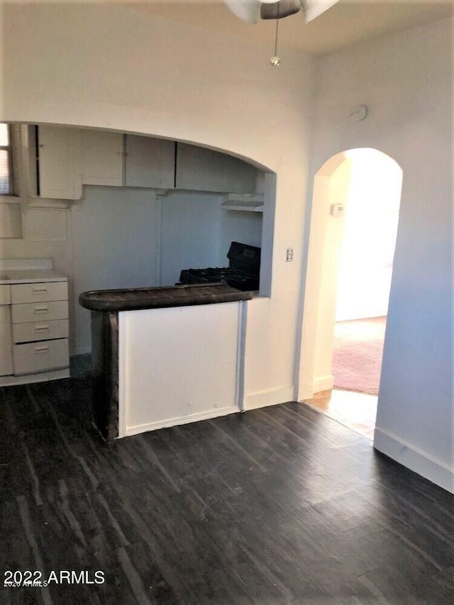 kitchen featuring baseboards, arched walkways, dark wood-type flooring, and gray cabinetry