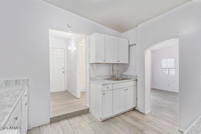 kitchen featuring baseboards, white cabinets, light wood-style flooring, light countertops, and a sink