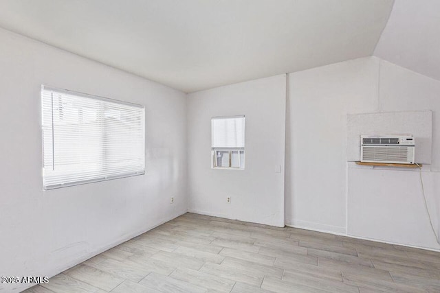 empty room featuring vaulted ceiling, an AC wall unit, and wood finished floors