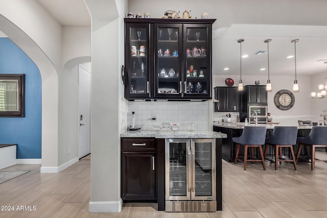 bar with pendant lighting, decorative backsplash, light wood-type flooring, light stone counters, and beverage cooler