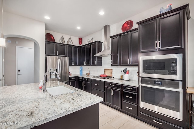 kitchen featuring pendant lighting, sink, wall chimney exhaust hood, light stone countertops, and appliances with stainless steel finishes