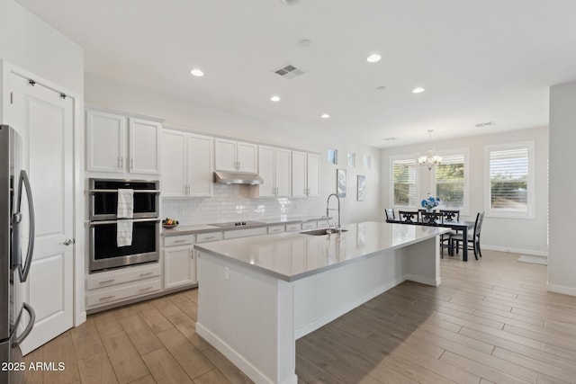 1294 E Ln Fortuna Ct, San Tan Valley, AZ 85140 - kitchen with under cabinet range hood, stainless steel appliances, light wood-style floors, light countertops, and a chandelier
